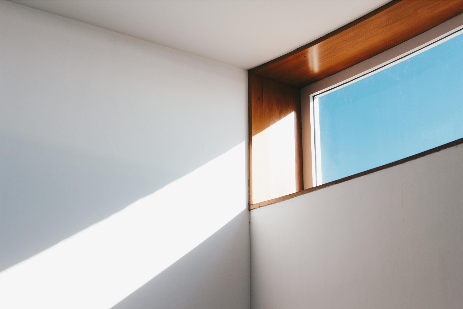 Corner of a bright sunny room showing a wooden window frame with light shining through it on to a white wall