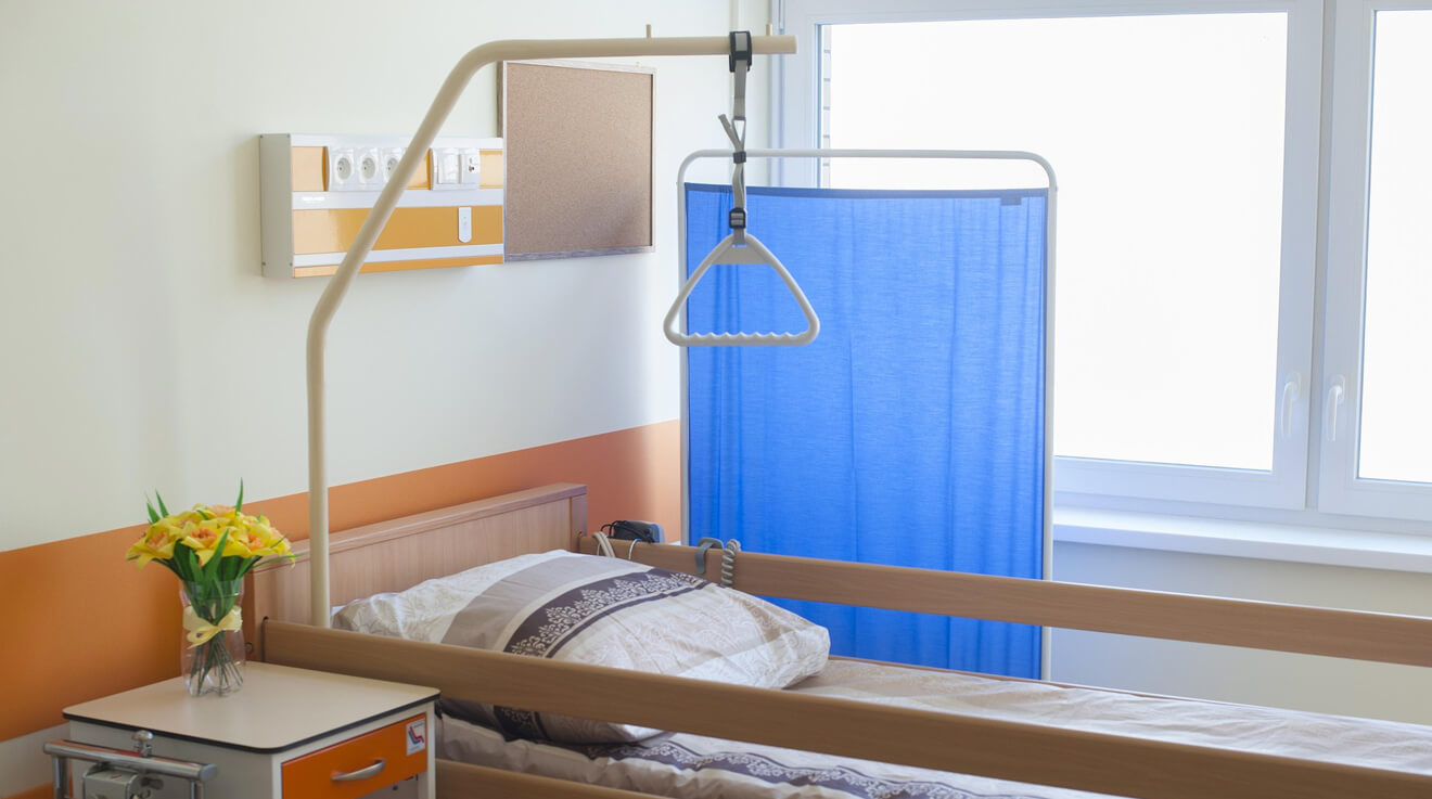 A hospital room containing a bed and privacy screen against a window with bright sunlight flooding in