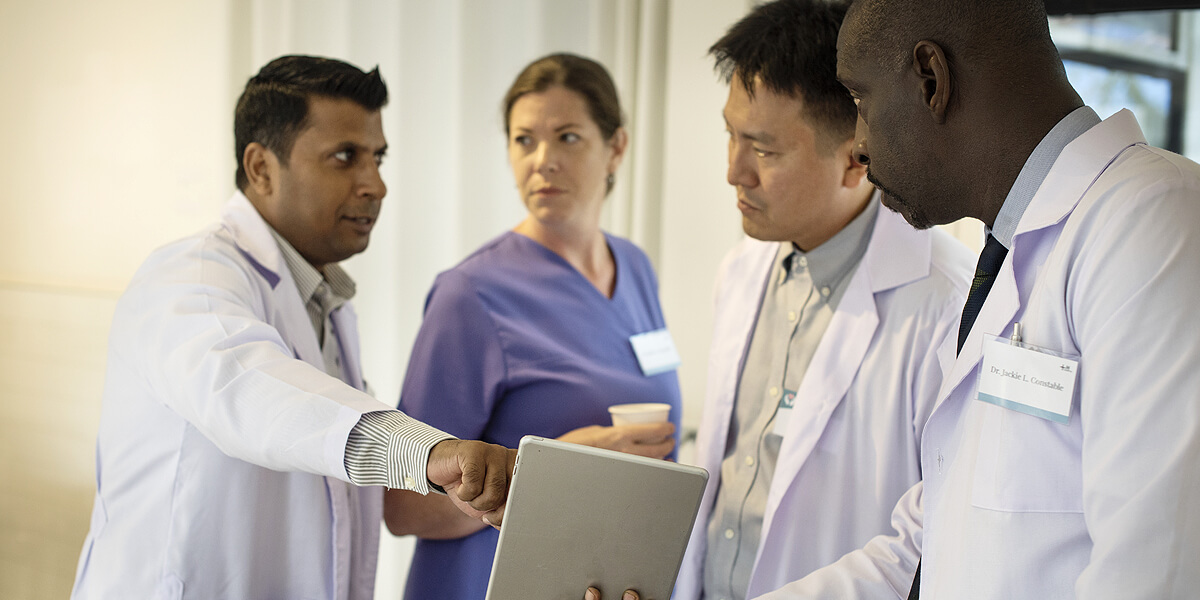 A diverse group of medical professionals in a hospital ward discussing results on a digital tablet device